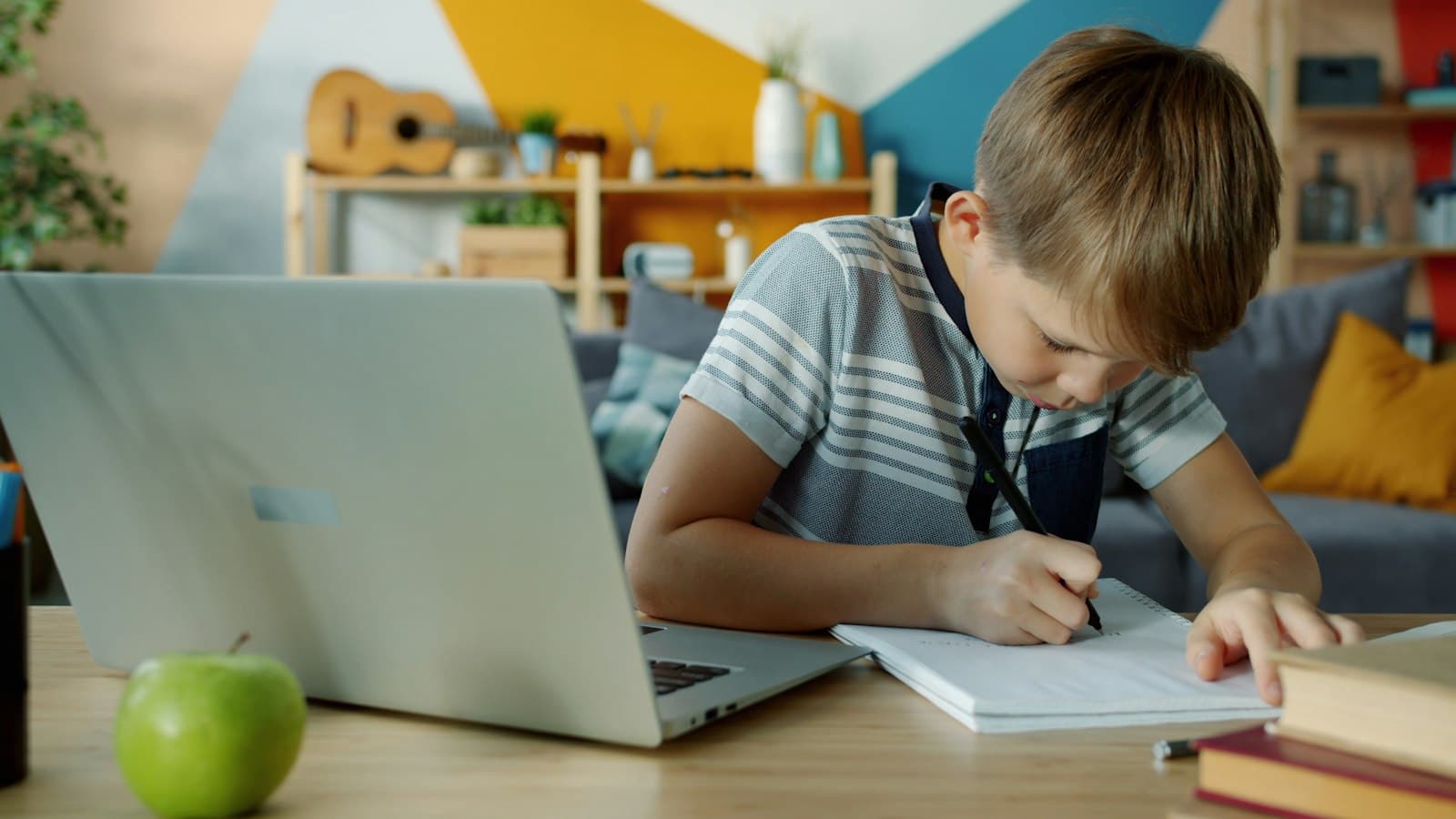 A boy doing his homework next to a laptop